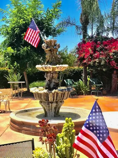 Beautiful outdoor garden area with a tiered fountain, lush plants, and American flags at Glory Days Assisted Care Living in Visalia.
