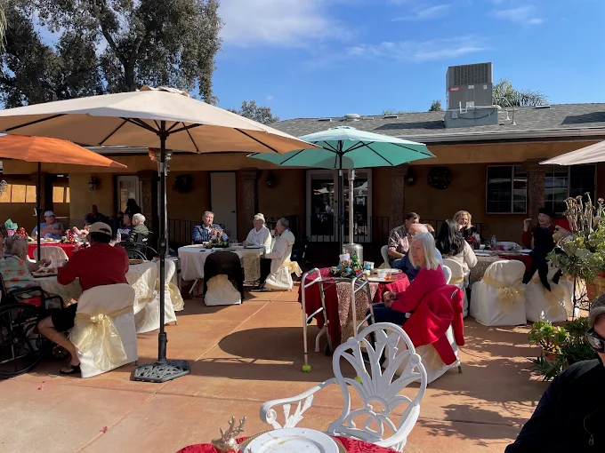 Residents and guests enjoying an outdoor luncheon or special event with parasols and dining tables in the comfortable, welcoming patio area of the Assisted Care Living facility.