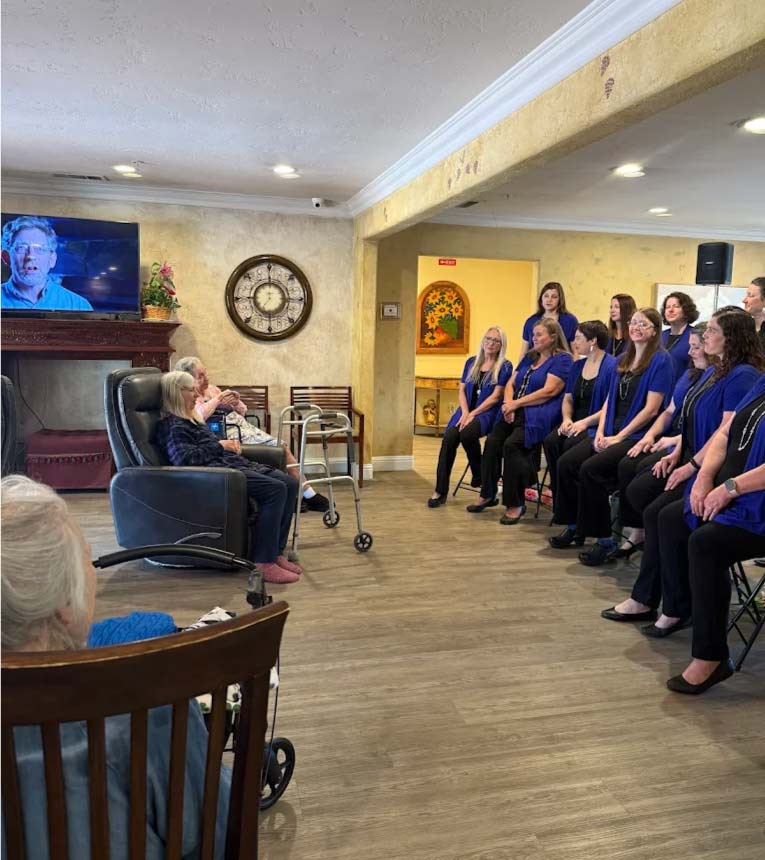Choir group in blue shirts performing live music therapy and entertainment for seated residents in the comfortable common area of an assisted living facility for personalized master care for seniors