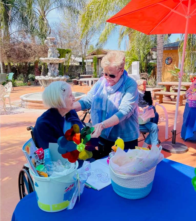 Family member visiting a senior resident in a wheelchair in the sunny outdoor garden courtyard at Glory Days senior living near me in visalia