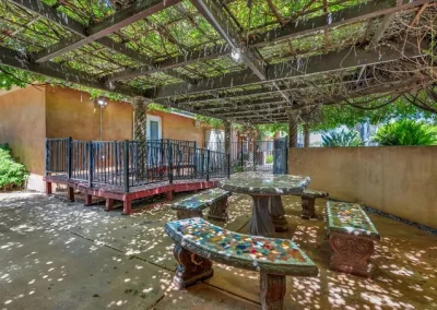 A peaceful garden courtyard at Glory Days with a vine-covered pergola, mosaic stone benches, and a secure fitness path for residents