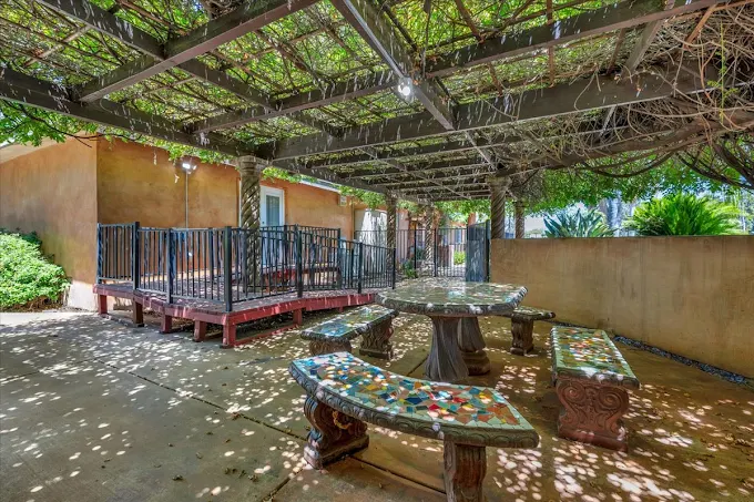 A peaceful garden courtyard at Glory Days with a vine-covered pergola, mosaic stone benches, and a secure fitness path for residents