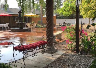 Beautiful outdoor courtyard at Glory Days assisted living featuring a stone water fountain, blooming flowers, and comfortable shaded seating areas for residents and visiting families.