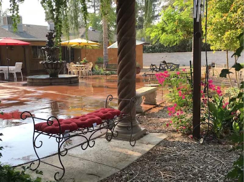 Beautiful outdoor courtyard at Glory Days assisted living featuring a stone water fountain, blooming flowers, and comfortable shaded seating areas for residents and visiting families.